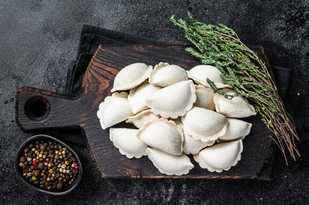 Frozen raw dumplings pierogi with potato on a wooden board. Black background. Top Viewの写真素材