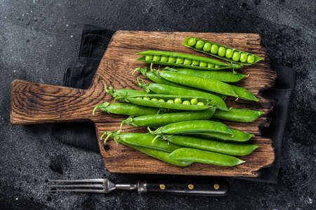 Fresh Peas and green pea pods on a wooden cutting board. Black background. Top view