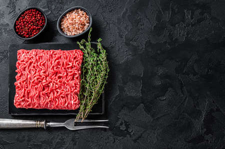 Fresh Raw Mince Ground beef meat with thyme. Black background. Top view. Copy space
