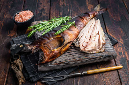 Cut Hot smoked fish on a wooden board with rosemary. Dark wooden background. Top view