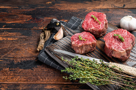 Prime raw Fillet mignon steaks on a wooden board with thyme and garlic. Dark wooden background. Top view. Copy spaceの写真素材