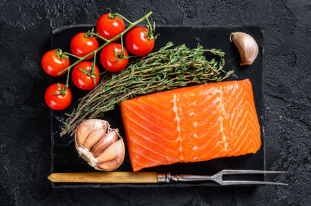 Protein vegetarian diet - raw salmon fillet steak with herbs and tomato. Black background. Top viewの写真素材