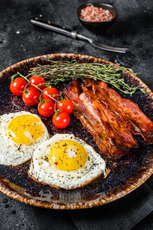 Breakfast with fried eggs and bacon with herbs in plate. Black background. Top viewの写真素材