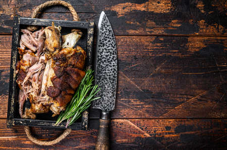 Roasted pork knuckle eisbein meat in a wooden tray with knife. Dark wooden background. Top view. Copy spaceの写真素材
