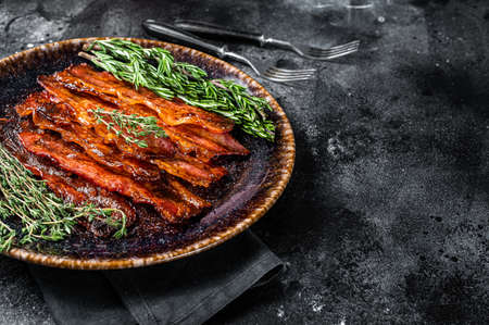 Hot Fried crunchy Bacon sizzling slices in plate with herbs. Black background. Top view. Copy spaceの写真素材
