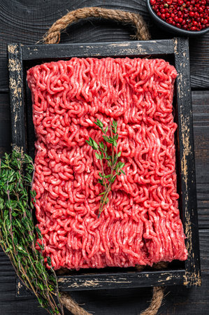 Raw mince ground beef and pork meat in a wooden tray with herbs. Black background. Top view