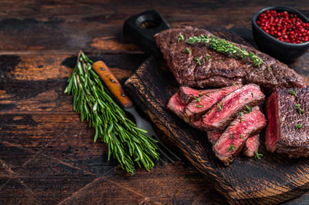 Grilled sliced skirt beef meat steak on a cutting board with herbs. Dark wooden background. Top view. Copy spaceの写真素材
