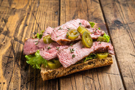Griiled Steak sandwich with sliced beef, rocket and vegetables on bread. Wooden background. Top viewの写真素材
