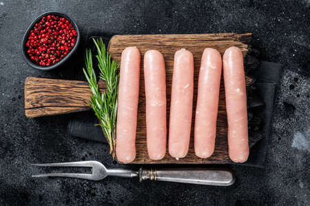 Fresh Raw chicken and turkey meat sausages on a wooden board with rosemary. Black background. Top viewの写真素材