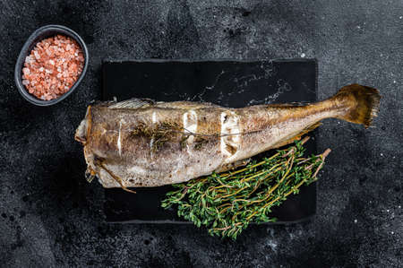 Roasted cod white fish with thyme on marble board. Black background. Top view