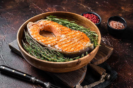 Roasted Salmon Trout Fish Steak in a vintage wooden plate with thyme and rosemary. Dark background. Top viewの写真素材