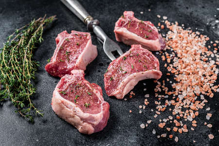 Raw lamb loin steaks, chops cutlets on kitchen table. Black background. Top view