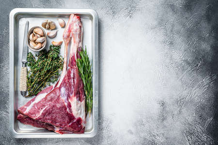 Uncooked Raw goat or lamb leg with herbs in baking tray. White background. Top view. Copy spaceの写真素材