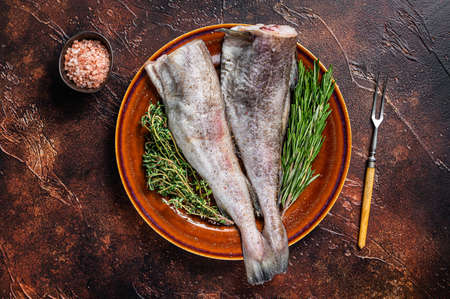 Uncooked Raw cod or codfish fish in rustic plate with herbs and fork. Dark background. Top viewの写真素材