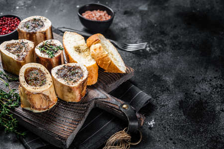 Roast marrow calf bones on wooden board with bread and herbs. Black background. Top view. Copy spaceの写真素材