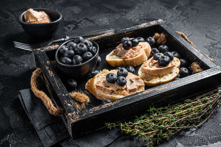 Foie gras toasts, duck liver pate and fresh blueberry in wooden tray. Black background. Top viewの写真素材