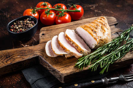 Roasted chicken breast fillet on a wooden board with herbs. Dark background. Top viewの写真素材