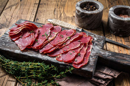 Dried Pastrami slices, beef meat with herbs on wooden board. Wooden background. Top viewの写真素材