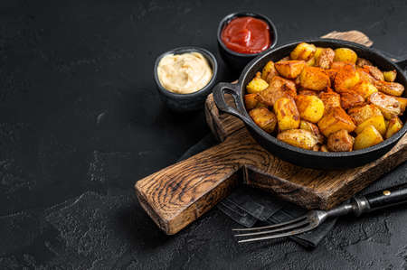 Patatas bravas, spicy potatoes, a Spanish dish with fried potato and a spicy garlic sauce. Black background. Top view. Copy spaceの写真素材