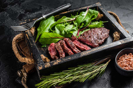BBQ roasted flank steak in wooden tray with vegetable salad. Black background. Top viewの写真素材