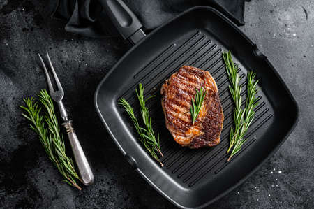 Roasted rib eye steak, ribeye beef meat in a grill pan. Black background. top viewの写真素材