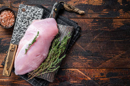 Raw turkey breast fillet on a wooden butcher board with meat cleaver. Dark wooden background. Top View. Copy spaceの写真素材