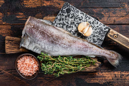 Fresh Raw cod or codfish fish on wooden board with cleaver. Dark Wooden background. Top view