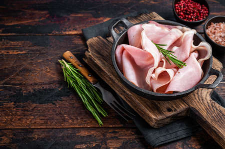 Prosciutto ham sliced in a pan. Dark wooden background. Top view. Copy space