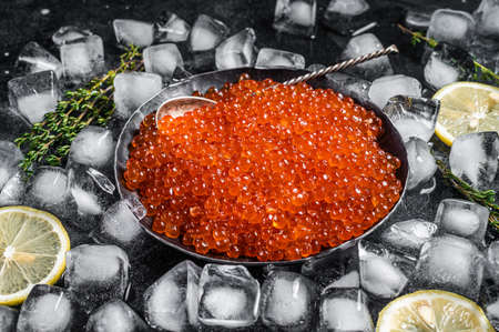 Salty Red caviar in steel plate on ice. Black background. Top viewの写真素材