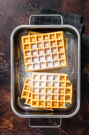 Viennese waffles with powdered sugar in kitchen steel tray. Dark background. Top view