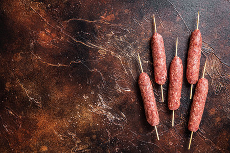 Raw kofta meat kebabs sausages on skewers. Dark background. Top view. Copy spaceの写真素材