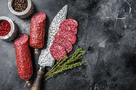 Traditional smoked salami cured sausage on kitchen table. Black background. Top view. Copy space