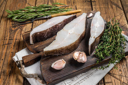 Atlantic halibut fish, raw steaks on wooden board with herbs. Wooden background. Top view
