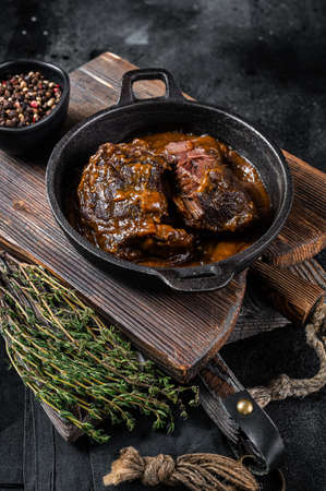 Stewed beef cheeks with brown red wine sauce in skillet. Black background. Top viewの写真素材