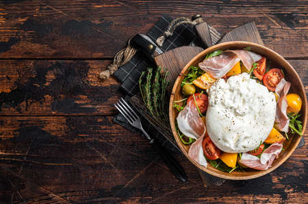 Italian tomatoes and burrata cheese salad with arugula, prosciutto ham and olives. Wooden background. Top view. Copy spaceの写真素材