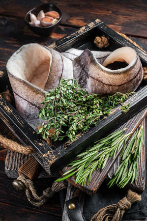 Raw Haddock fish fillets in wooden tray with rosemary and thyme. Wooden background. Top view