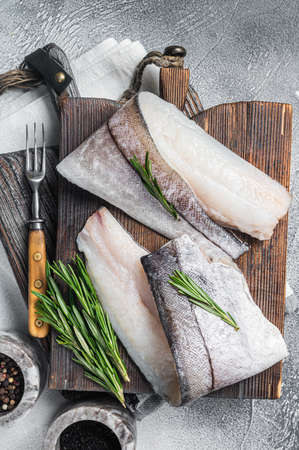 Haddock fish fillet, raw seafood meat on wooden board with herbs. White background. Top viewの素材 [FY310180266667]