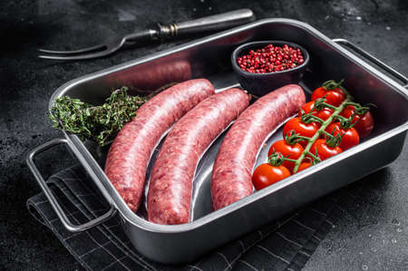 Uncooked Raw lamb and beef meat sausages in kitchen tray with herbs. Black background. Top viewの写真素材