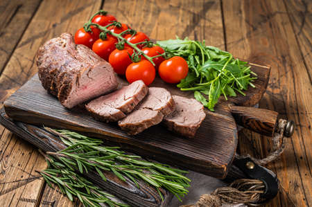 Roast Veal tenderloin, sliced Roastbeef on wooden board with garnish. Wooden background. Top viewの写真素材