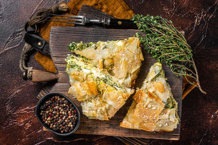 Spanakopita Greek Pie with Spinach and Cheese on wooden board. Dark background. Top view