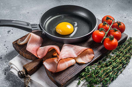 Cooking fried Egg in a skillet with bacon and tomato. Gray background. Top viewの写真素材