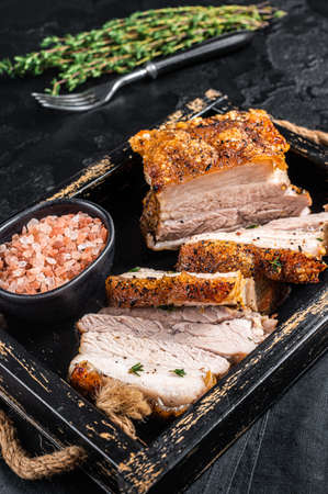 Crispy Roast Pork Belly. Sliced roasted meat with crust in a tray with spices. Black background. Top viewの写真素材