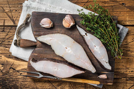 Atlantic halibut fish, raw steaks on wooden board with herbs. Wooden background. Top viewの写真素材