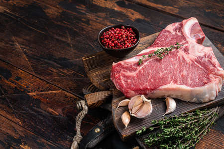 Prime T-bone beef meat steak, raw porterhouse steak on butcher board with herbs. Wooden background. Top view. Copy spaceの写真素材