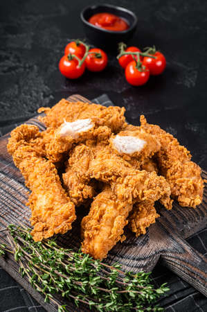 Dip fried Breaded chicken breast strips with tomato ketchup on a wooden board. Black backgrund. Top viewの写真素材