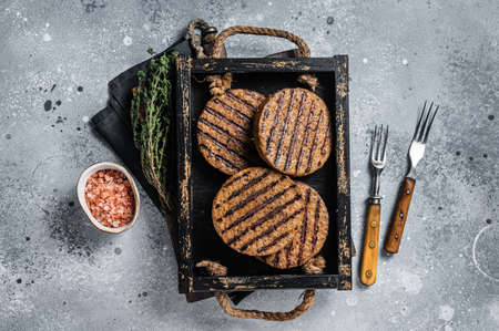 Roasted meat free patties, plant based meat burger cutlets in wooden tray with herbs. Gray background. Top viewの写真素材