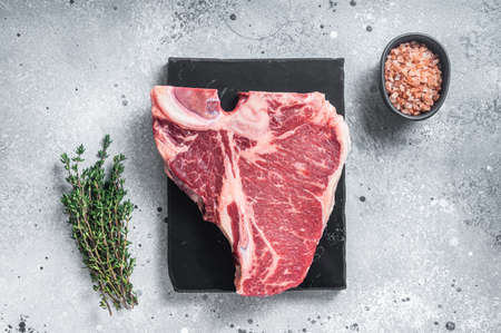 Raw dry aged wagyu porterhouse beef steak, uncooked T-bone on marble board with thyme. Gray background. Top viewの写真素材
