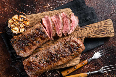 Grilled Lamb sirloin fillet meat on wooden board with herbs, mutton loin steak. Dark background. Top view.の写真素材