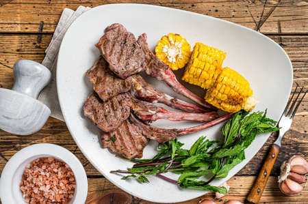 Grilled lamb chops steaks in a plate with corn and tomato. wooden background. Top view