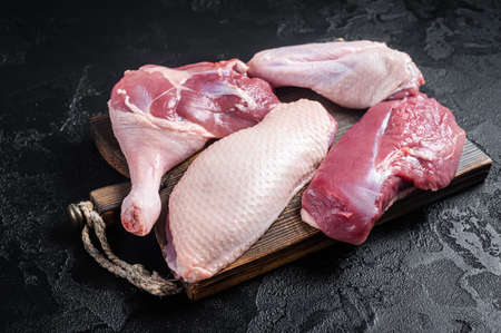 Duck breast fillet, legs, wings, raw meat on a butcher cutting board. Black background. Top viewの写真素材